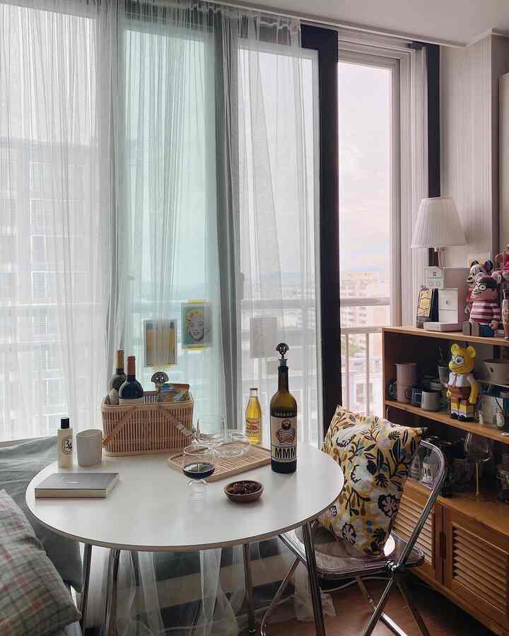 白と木目調が調和するキッチン空間、透明な椅子とワイングラスが置かれた丸いダイニングテーブルが雰囲気のあるインテリアを演出。