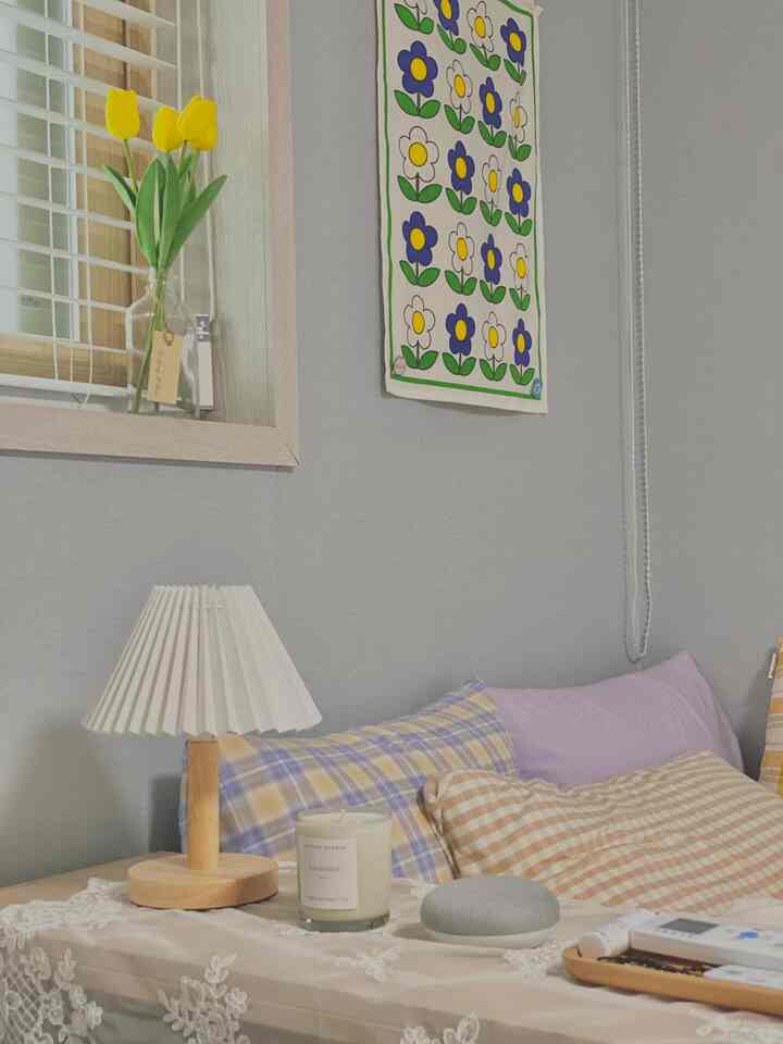 Lavender and white toned bedroom featuring checkered pillow covers, a table lamp, and a scented candle creating a cozy atmosphere