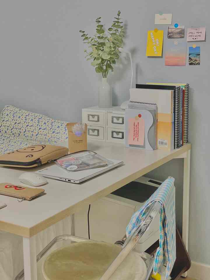 Pastel sky blue toned small home office space featuring a white desk, transparent chair, organized notebooks, and a decorative plant with a clean atmosphere