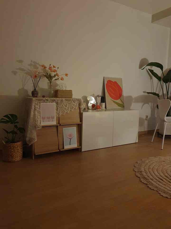 ナチュラルな色調のリビング空間、木製収納と白いキャビネットに花や植物、レースが配置された雰囲気のあるインテリア