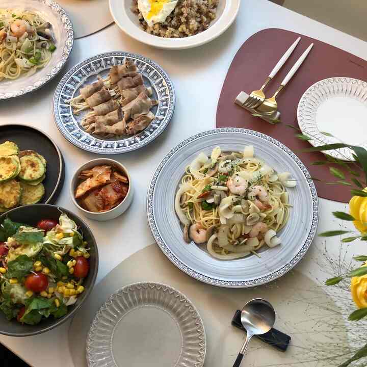 白を基調としたダイニング、デスカーのテーブルに多様な皿やボウルが並び、ホームパーティーの雰囲気が感じられるインテリア