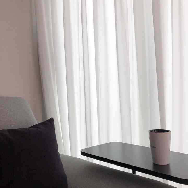 White sheer curtains with a gray fabric recliner and black side table in a simple and cozy living room space