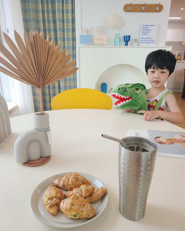 Warm children's room with a white round dining table, yellow chair, and a child holding a dinosaur toy