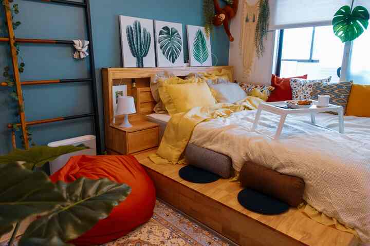 木目調のベッドと黄色い寝具が印象的な寝室、ビーズクッションと多様なクッション、白いベッドトレイが配置された居心地の良い空間