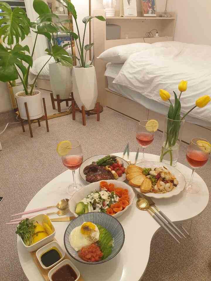 White and beige toned studio bedroom featuring a cozy table set with home cafe style meal and bright yellow tulips