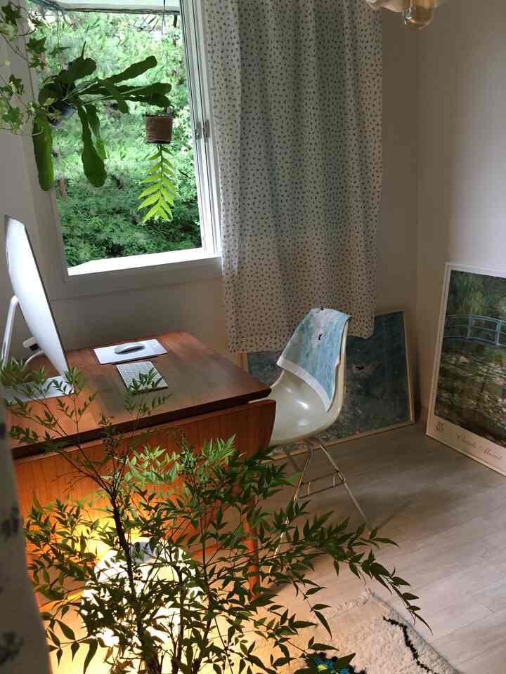 白と木目調のホームオフィス、窓際に植物と額縁が配置された自然な雰囲気のある印象的な空間