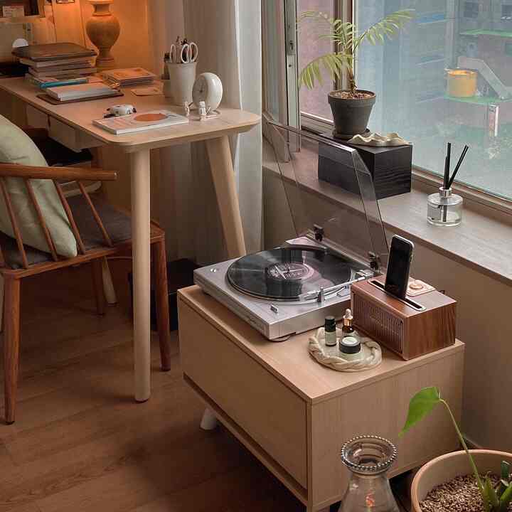 ベージュと木目調の書斎、窓際のナイトテーブルの上にターンテーブルと植物が配置された雰囲気のあるナチュラルモダンなインテリア