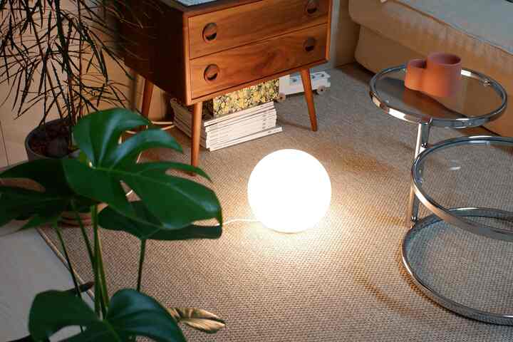 Natural-toned living room featuring monstera plant, wooden nightstand, and bright spherical table lamp creating a cozy atmosphere