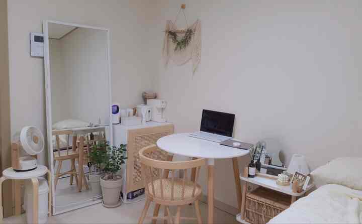 Compact single household living room in white and wood tones featuring round table, rattan chair, and houseplants with a simple atmosphere