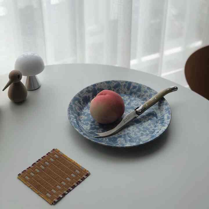 白いトーンの丸いダイニングテーブルに青い模様の皿、桃、ラギオールのカトラリーが置かれた清潔感のあるおうちカフェの雰囲気のあるインテリア