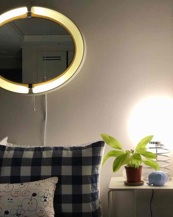 Bedroom with white walls and lighting featuring checkered cushions and a plant on a side table, creating a cozy atmosphere