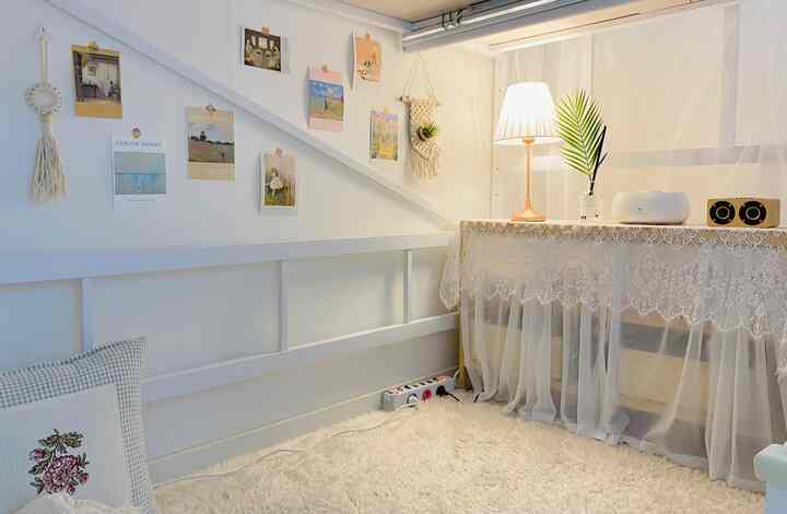 Natural tone small room in white, featuring art posters and macrame on walls, floor lamp and lace-covered table with cozy atmosphere