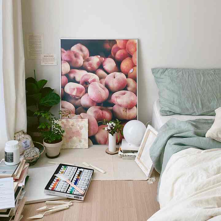 ナチュラルカラーの寝室、窓辺に植物とポスター、緑の寝具が配置された落ち着いた雰囲気のインテリア