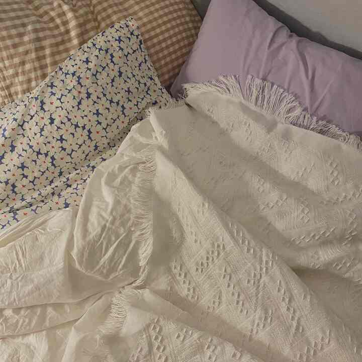 White and beige toned bedroom featuring various patterned blankets and pillows in a cozy setting