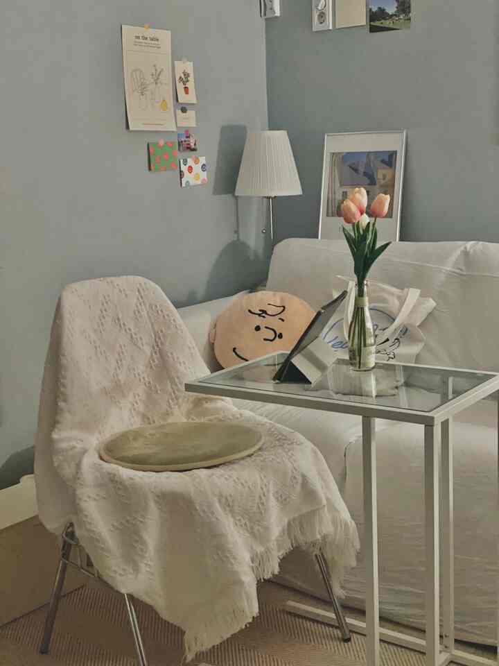 A cozy living room with soft blue walls, white sofa, covered armchair, side table, and a vase with flowers