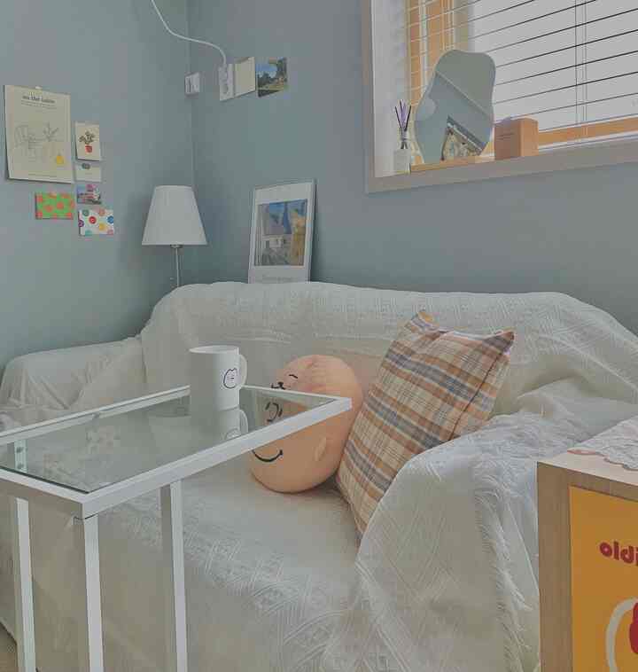 白いソファカバーがかかったリビング、チェック柄クッションと笑顔のクッションが置かれた温かみのある空間