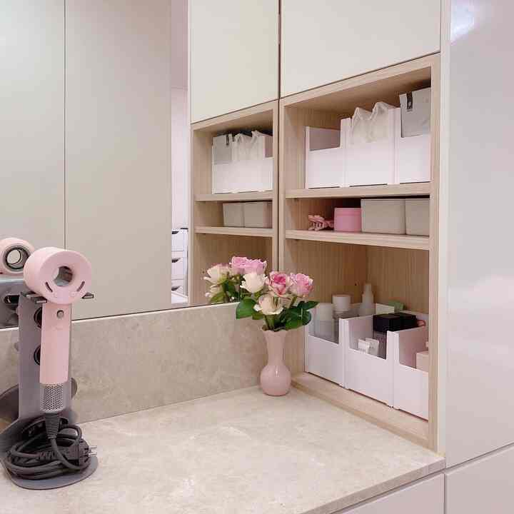 White and wood tone built-in vanity closet with pink accents, featuring organized storage boxes and a sleek countertop