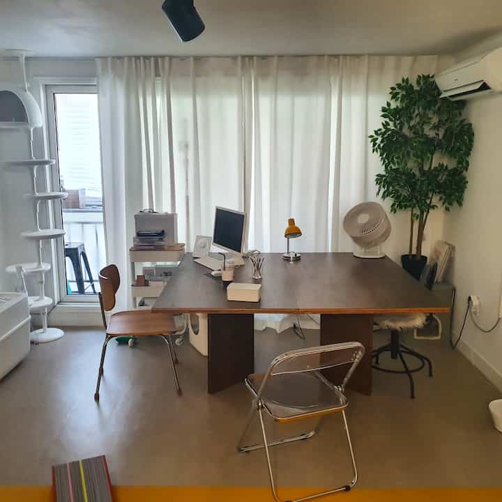 White and wood-tone dining room featuring mid-century modern furniture and a cat tower in a minimalist home office space