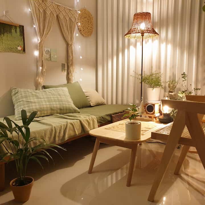 ナチュラルな木目調と緑の植物が調和するヴィンテージスタイルのリビング、ラタン照明とソファベッドが温かみのある雰囲気を演出するインテリア