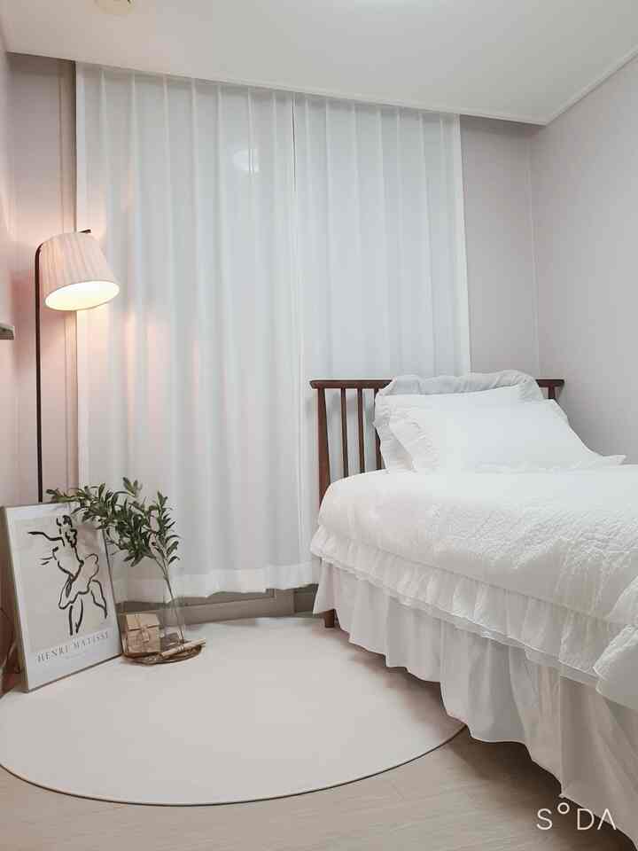 White and natural toned bedroom featuring wooden bed frame, ruffled bedding, and soft curtains creating a simple cozy atmosphere