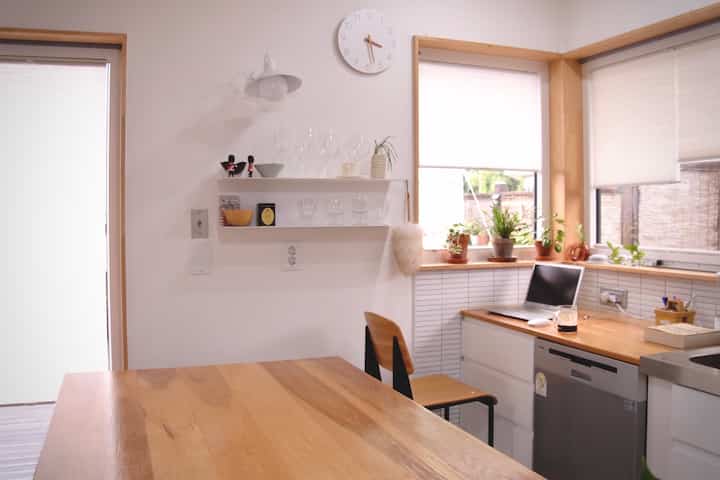 Natural wood tone and white kitchen and dining space featuring wooden table, chair, shelves with clean and cozy atmosphere