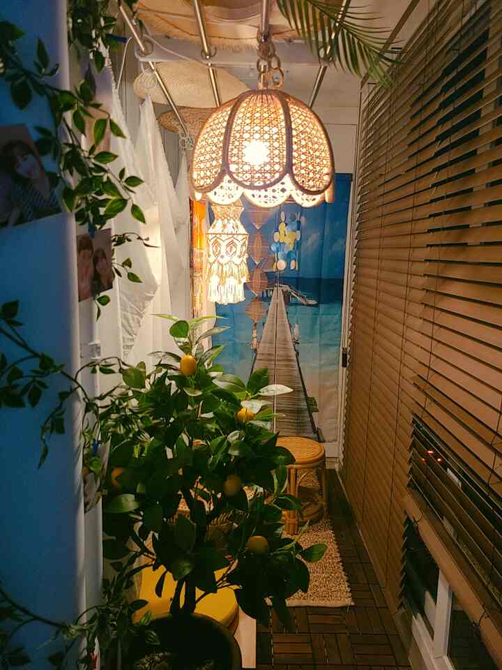 温かみのある木目調とラタン照明が配置されたベランダ、植物とカーテンが飾られた雰囲気のあるインテリア