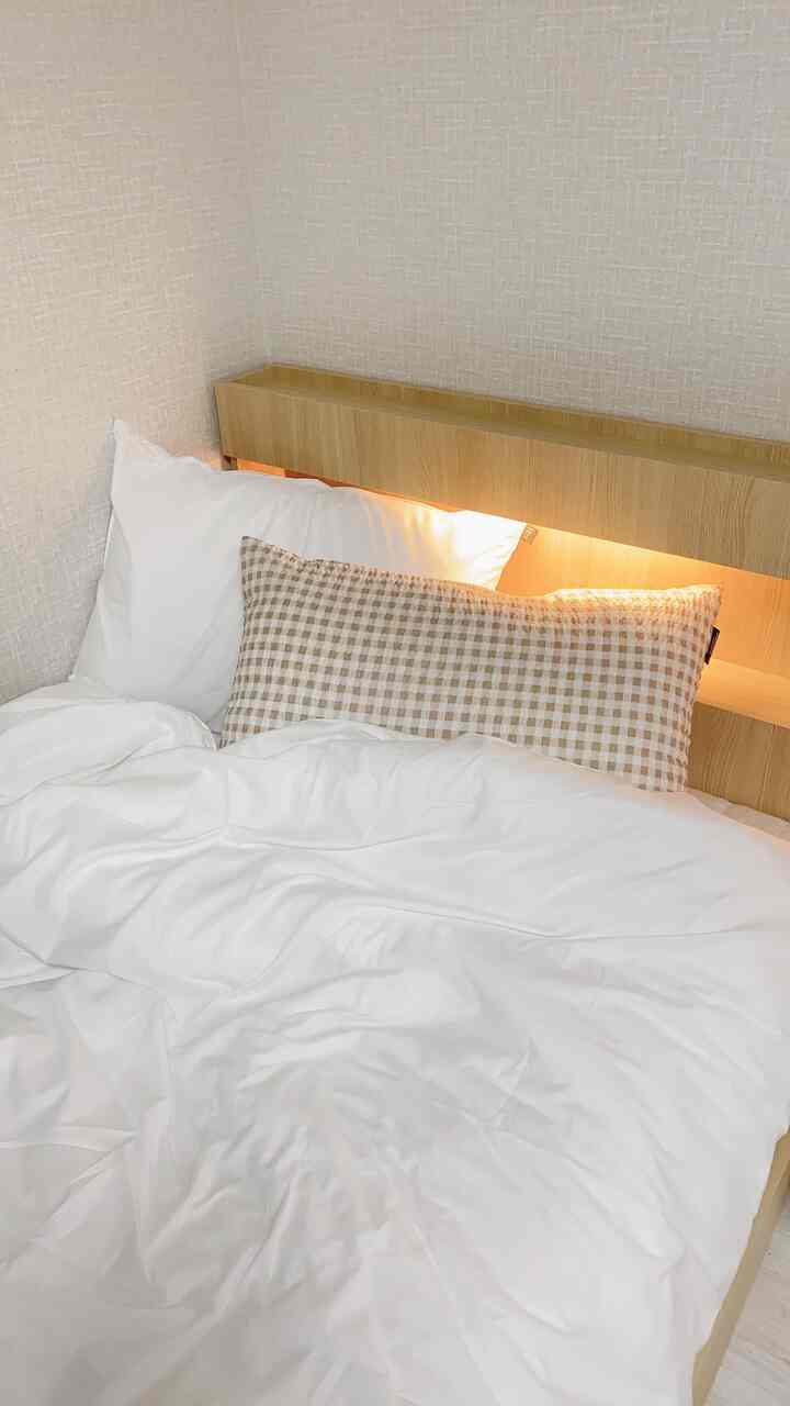 Bright wood-tone headboard with white bedding and beige check pillows in a clean bedroom space