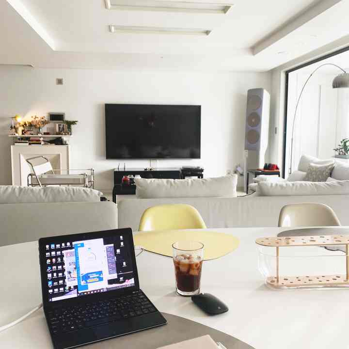 White-toned dining room in mid-century modern style featuring dining table, chairs, laptop, and iced coffee creating a cozy workspace