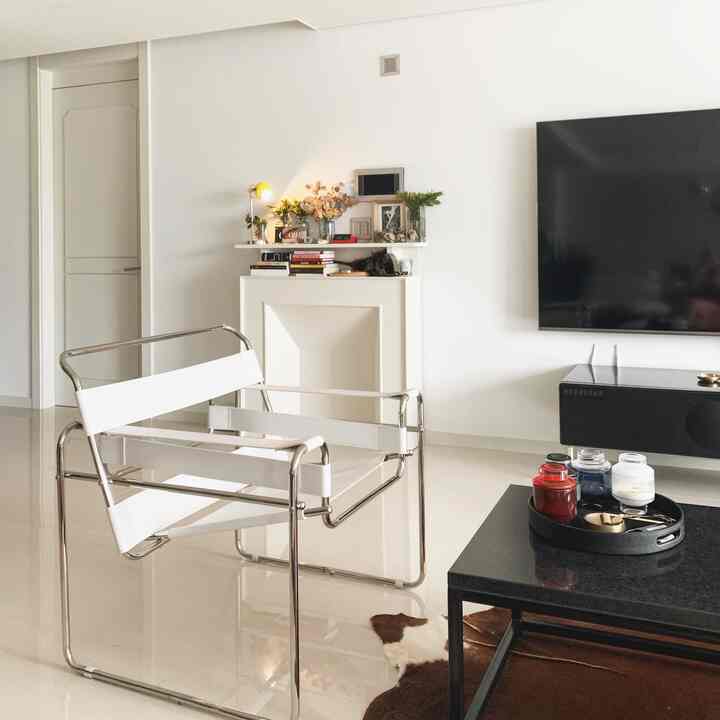 White-toned living room featuring a modern metal armchair, black coffee table with a tray, and a wall-mounted TV, creating a clean and sleek atmosphere