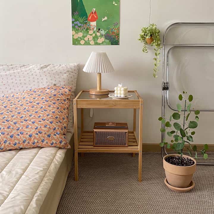 白い壁と木目調のナイトテーブルがあるナチュラルスタイルの寝室、ベッドと植物が配置された雰囲気のあるインテリア