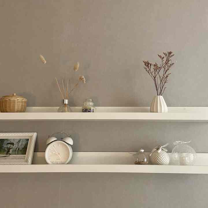 A modern and simple bedroom wall with gray background featuring white shelves neatly arranged with calm decorative items