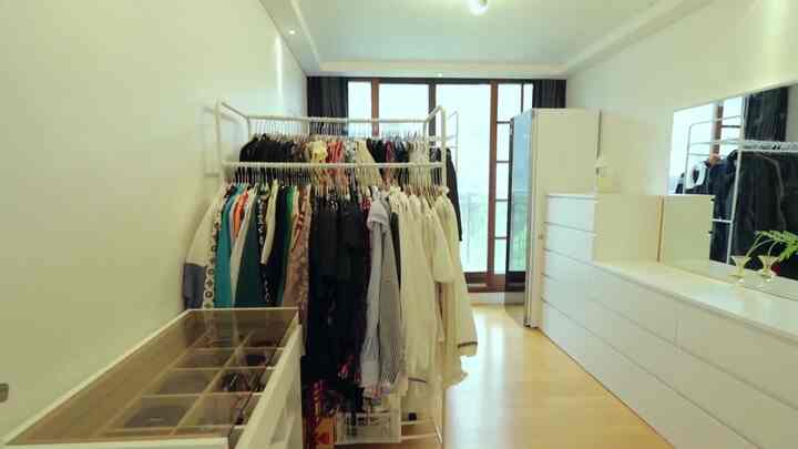Bright and organized walk-in closet in white and wood tones featuring a rolling garment rack and dresser
