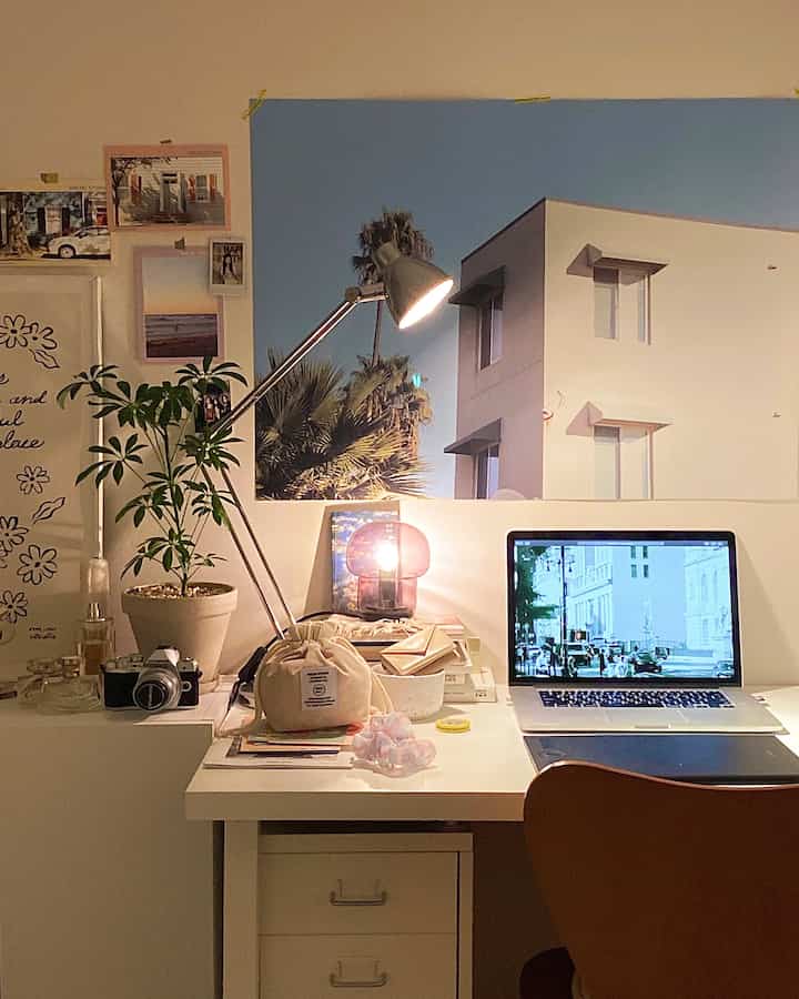 White-toned home office space featuring a clean desk, dresser, lamps, and a poster creating a cozy working area