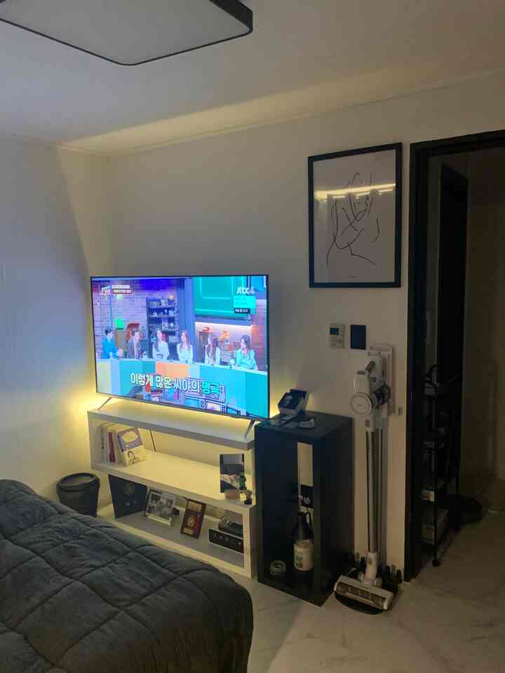Modern living room with white walls and ceiling, featuring a black sofa and large TV creating a cozy atmosphere