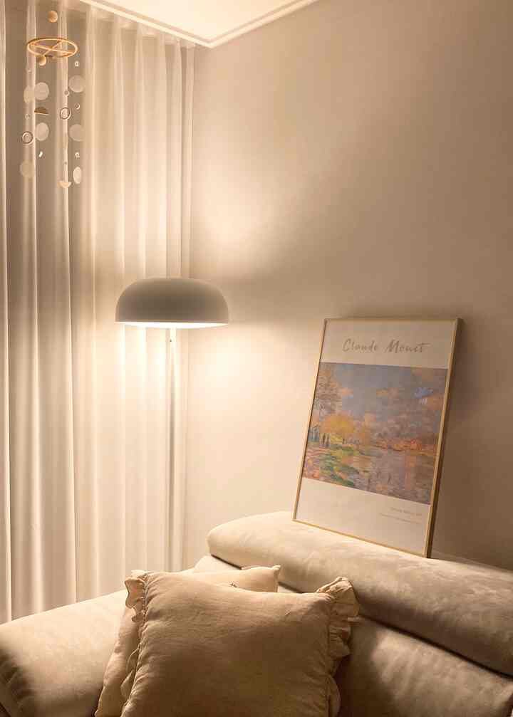 Soft beige-toned living room featuring a beige sofa, floor lamp, mother-of-pearl mobile, and warm lighting creating a cozy space