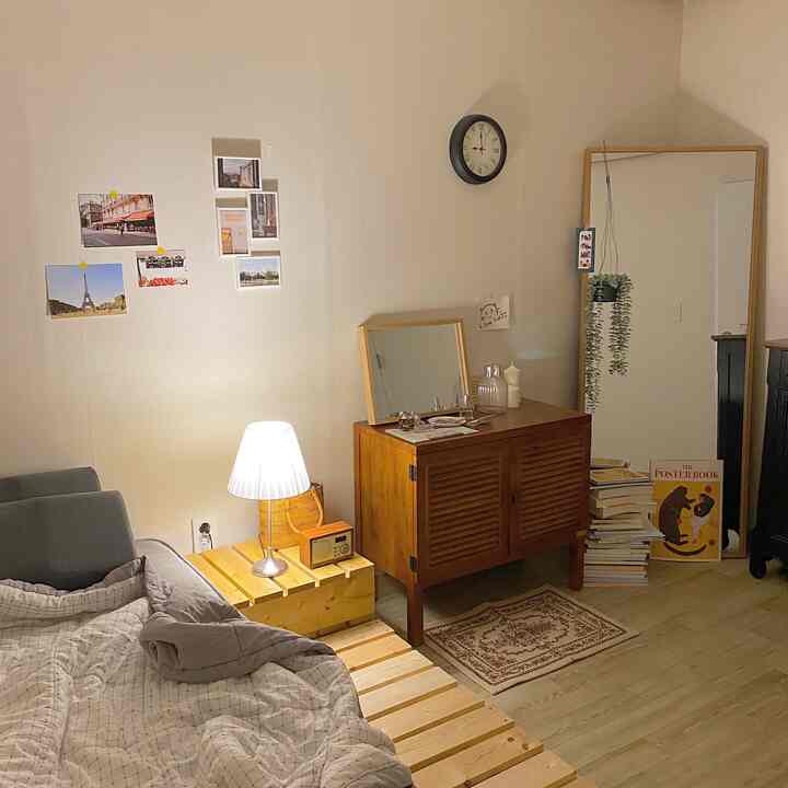 Warm wood-toned bedroom with beige walls, featuring a natural wood bed frame, wooden dresser, wall clock, and soft lighting creating a cozy atmosphere