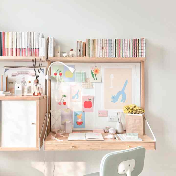 Natural home office space with white walls and wood tone furniture, featuring playful posters and bookshelves on the wall