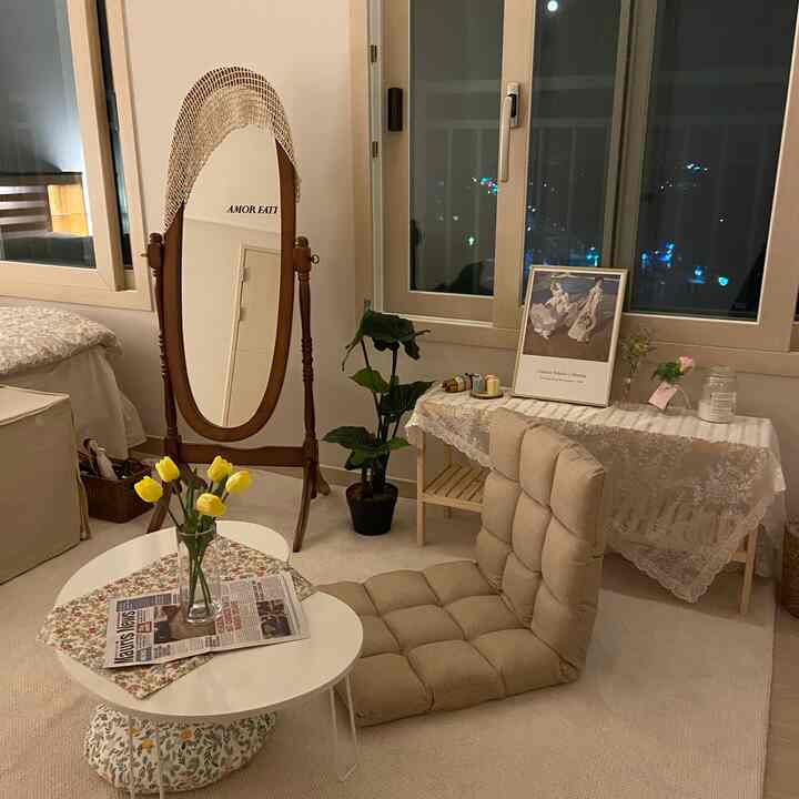 Soft beige and wood tone living room featuring cafe-style table and chair, vase with flowers, and lace tablecloth creating a cozy space
