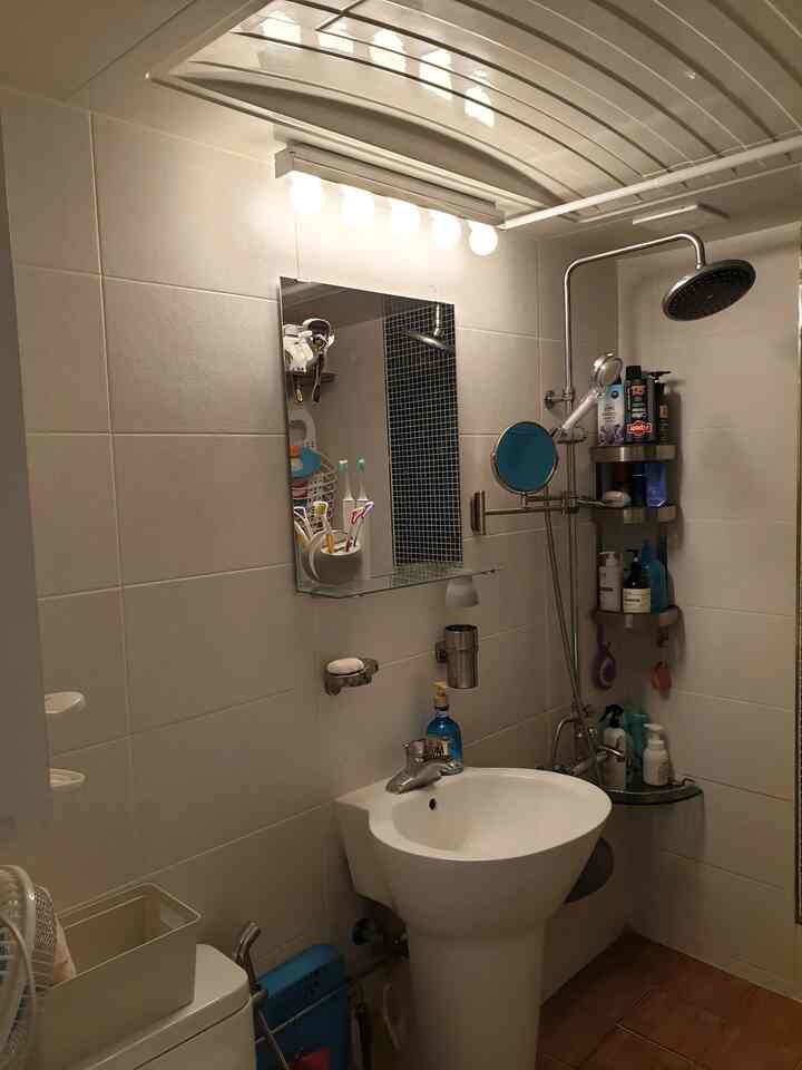 ホワイトの壁とブラウンの床タイルがある小さなバスルーム、壁付ライトと鏡、コーナーシェルフが配置されたシンプルで清潔感のあるインテリア