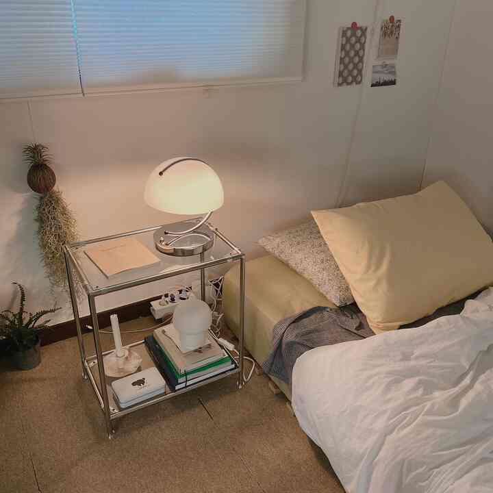 A white and beige toned studio apartment bedroom featuring a transparent nightstand and yellow pillows, creating a cozy atmosphere