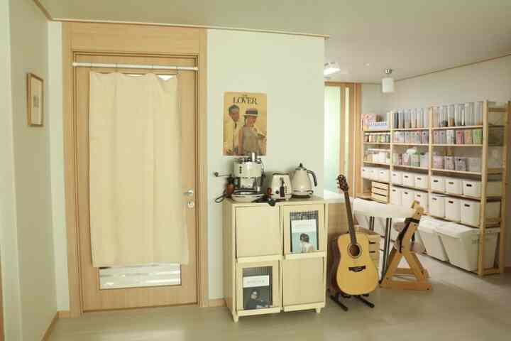 A bright beige and wood-tone pantry and home cafe space featuring organized storage shelves, a coffee setup, and a vintage poster creating a cozy interior