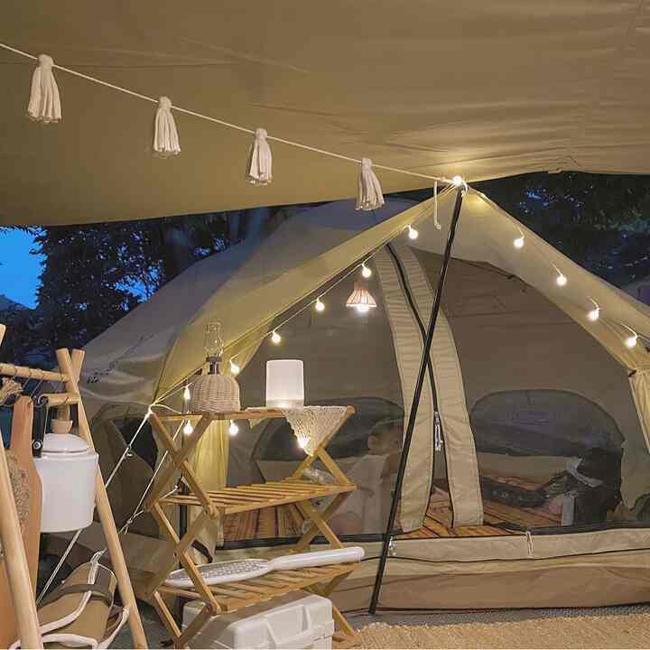 ベージュのテントとウッドトーンの棚、感性あふれるストリングライトが配置されたキャンプの雰囲気ある空間