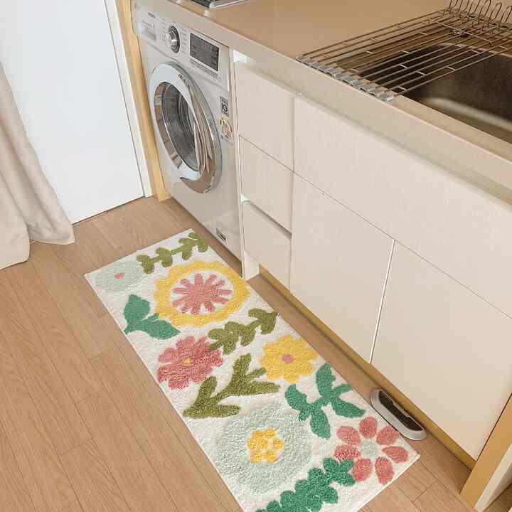 白とナチュラルカラーのキッチン、花柄のバスマットが置かれた清潔感のある印象的な空間