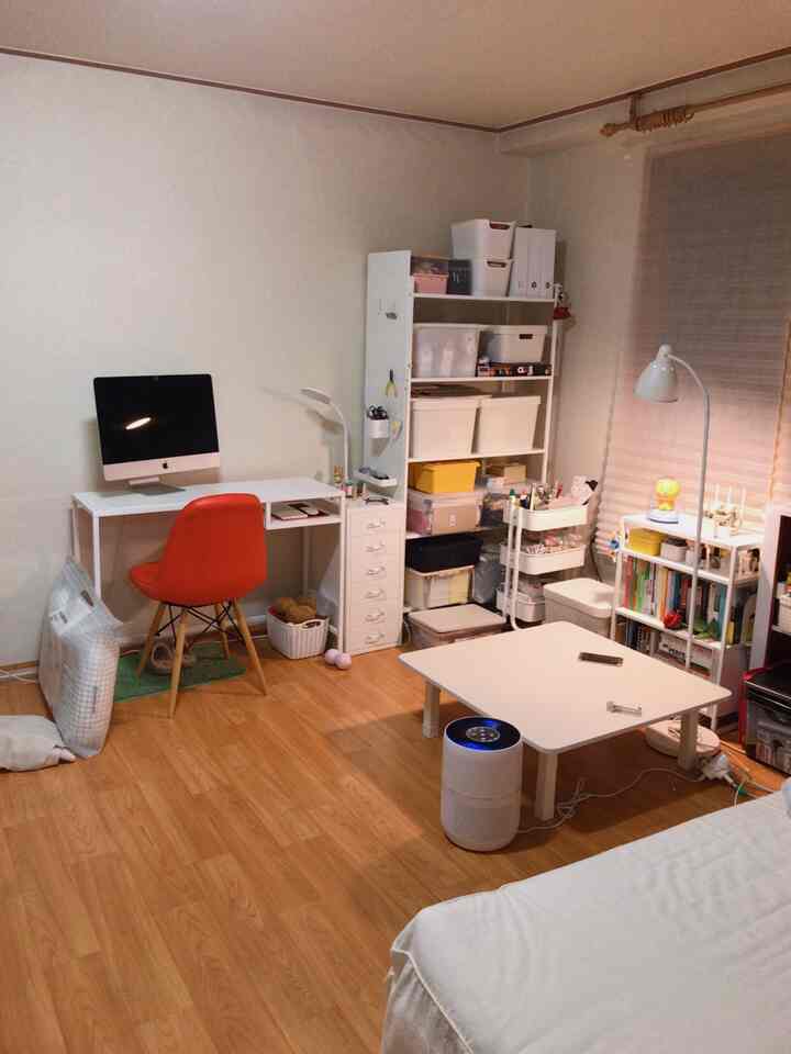 White and natural toned studio apartment featuring a desk, shelves, and floor lamp in a cozy, simple modern living workspace