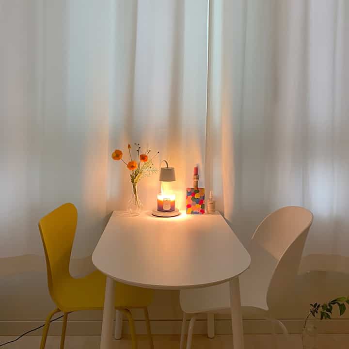 White-toned studio apartment featuring yellow chair, semi-circular table, and warm accent lighting creating a cozy home vacation vibe