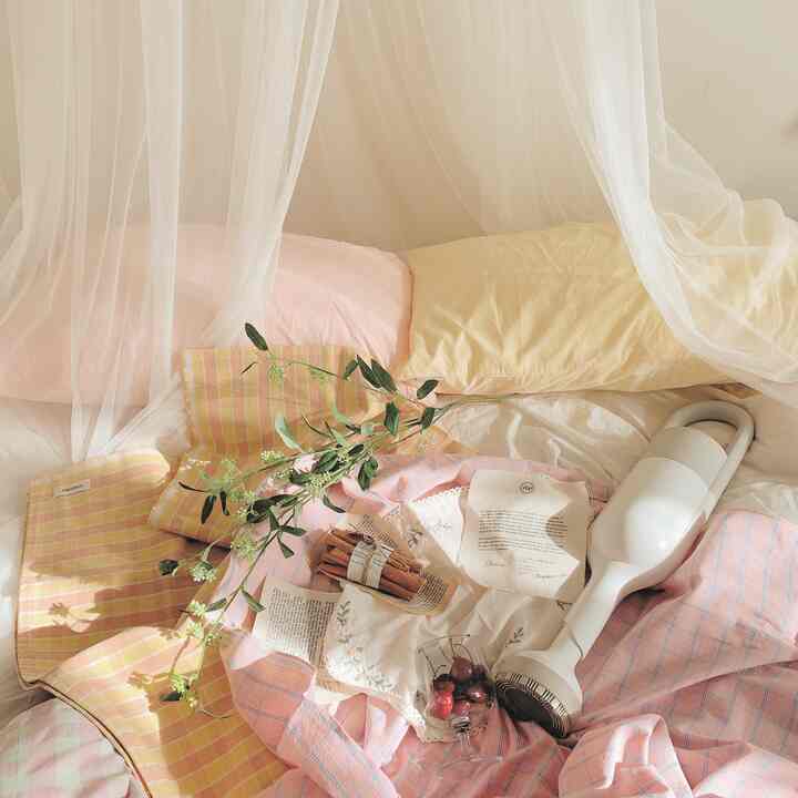 ホワイトとピンクの配色の寝室、ボヘミアン風レースのキャノピーと多彩な寝具が調和した雰囲気のあるインテリア