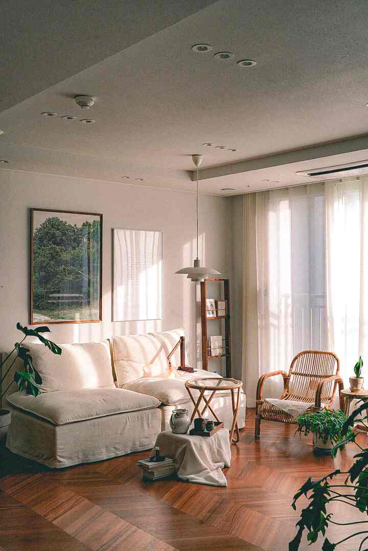 Bright white and wood tone living room featuring a modular sofa, rattan chair, plants, and chevron-patterned wooden floor in a cozy setting