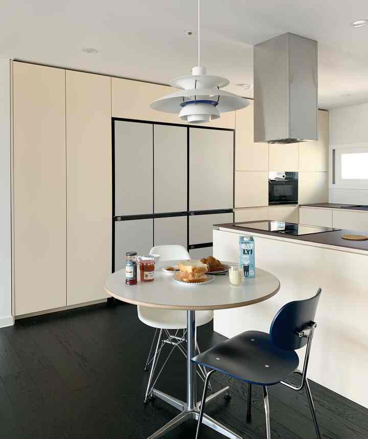 Modern kitchen in white tones featuring a round dining table with two chairs and a pendant light in a clean setting