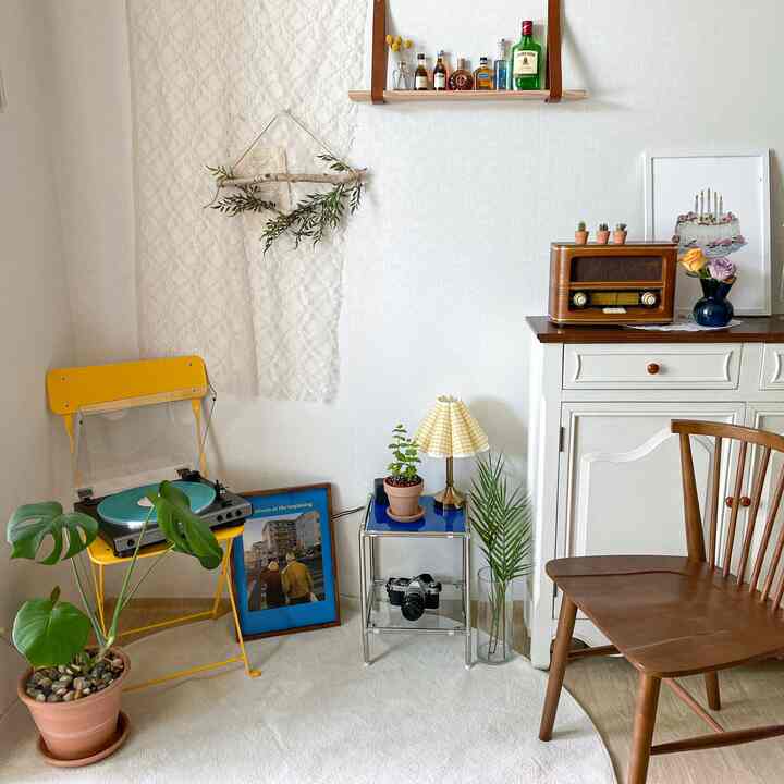 Cozy home cafe space featuring white walls and light brown wooden furniture, with a yellow chair holding a turntable, retro radio, and green plants arranged
