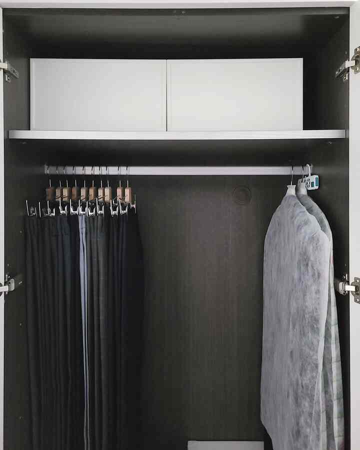 Dark wood-toned wardrobe featuring white storage boxes and black hangers with clothing, showcasing a tidy closet space
